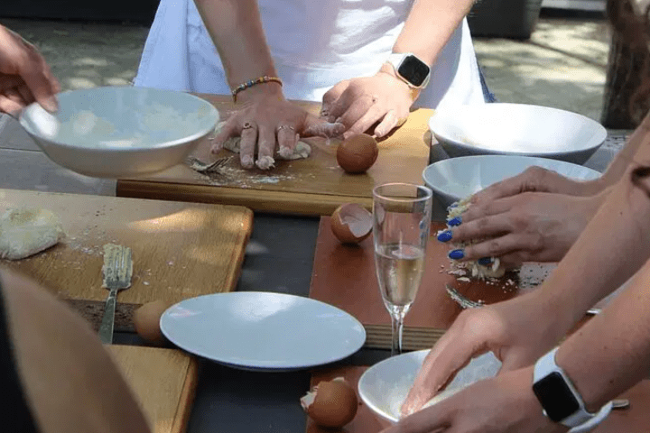 People kneading dough at a table with eggs, bowls, and a glass of champagne.