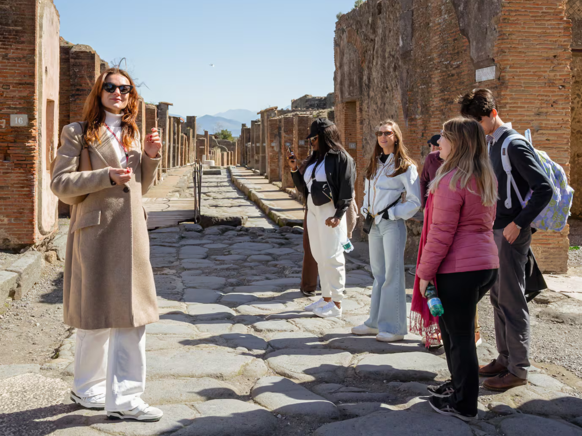 Tour guide with group in ancient ruins with cobblestone path and brick walls.