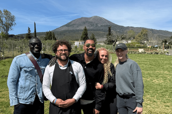 Five people smiling in front of a mountain on a sunny day.