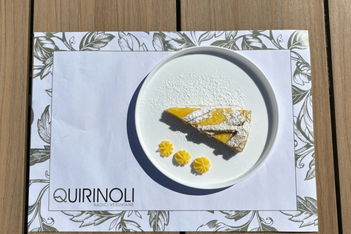 Slice of yellow cake with powdered sugar and three yellow dollops on a plate, on a floral placemat.