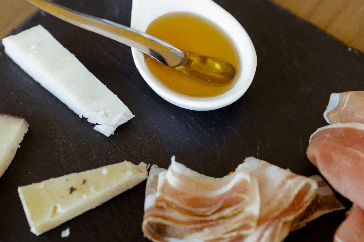 Slices of cheese and ham with a spoon in honey on a slate board.